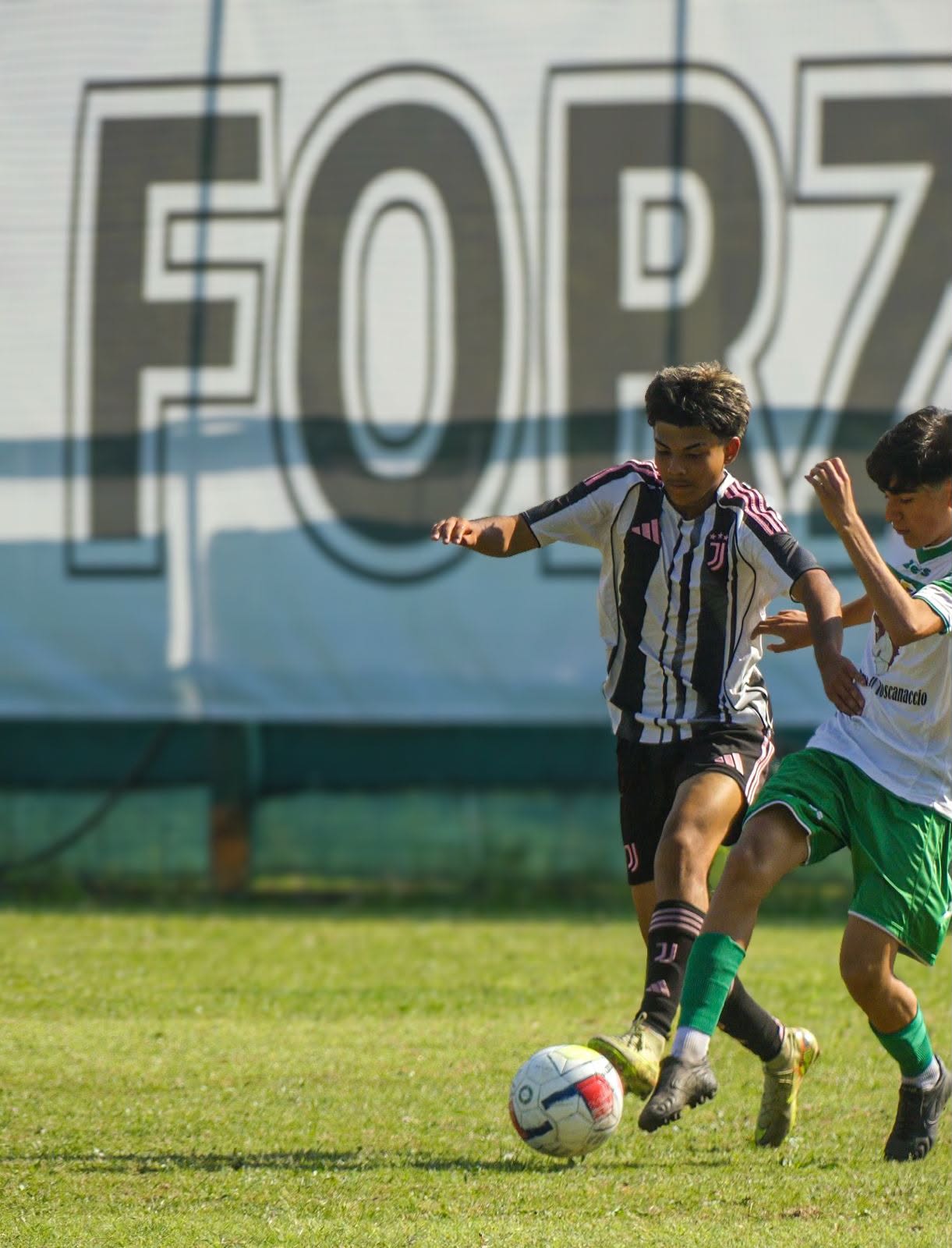 Eric on the ball against a defender in front of Forza banner